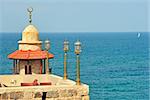 Small restaurant's stone balcony with lanterns and minaret of old mosque against background of Mediterranean sea in Yafo, Israel.