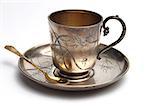 Antiquarian silver cup with a saucer and a  spoon on a white background