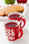 Christmas mulled wine in two small red cups and gingerbread and baubles on white background