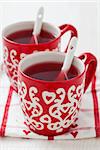 Christmas mulled wine in two small red cups resting on teatowel against white background