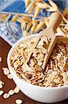 Oat flakes in a bowl witn wooden scoop close up.