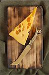 Piece of cheese and knife on an old cutting board.