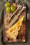 Piece of cheese, grape and nuts on an old cutting board.