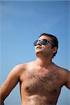 Indian Happy young man getting out of the water with sunglasses under blue sky