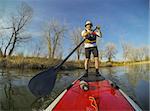 mature male paddler on a red stand up paddleboard (SUP), calm lake in Colorado, early spring