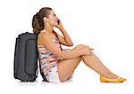 Young tourist woman with wheel bag sitting on floor and talking cell phone