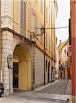 narrow cobblestone street lined with archways and yellow buildings, Modena, Italy