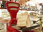 large wedge of parmesan cheese on red antique weigh scale in specialty meat and antipasto shop, Modena, Italy