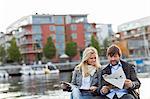 Couple sitting by water and reading newspaper