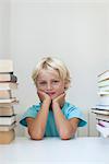 Boy sitting between tall stacks of books, portrait