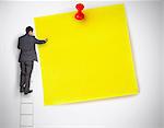 Businessman standing on ladder writing on large yellow note