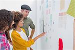 Smiling team of designers working together and pointing at a wall