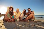 Smiling friends  sitting on the beach with beers