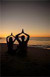 Silhouettes of people practicing yoga sat on the sand