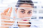 Delighted businesswoman peeking through a venetian blind