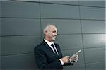 Mature businessman standing in front of wall, looking at tablet computer