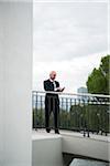 Mature businessman standing on bridge, looking at smartphone, Mannheim, Germany