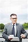 Portrait of mature businessman standing on bridge holding documents, wearing horn-rimmed eyeglasses, Mannheim, Germany