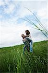 Mature couple in field of grass, man giving piggyback ride to woman, Germany