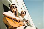 Young women sitting outdoors, hanging out and playing guitar, looking at camera, Mannheim, Germany