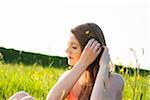 Young woman sitting in field placing flower in hair, Germany