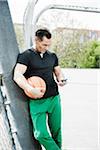 Mature man standing on outdoor basketball court looking at MP3 player, Germany