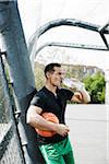 Mature man standing on outdoor basketball court drinking bottle of water, Germany