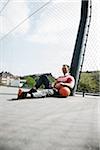 Mature man sitting on outdoor basketball court holding MP3 player, Germany