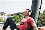 Mature man sitting on outdoor basketball court wearing headphones and listening to music, Germany