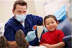Dentist and young patient smiling after checkup examination. The dentist is handing a lollipop to the young male patient. Both subjects are smiling toward the camera.