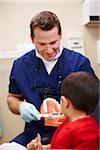 Male dentist showing young patient correct brushing technique.