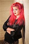 Punk female in leather jacket leaning against a wall