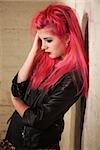 Depressed young woman with pink hair leaning against a wall