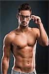 Shirtless male model posing with glasses over a blue background