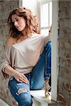 Attractive young woman sitting on the window sill