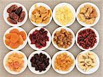 Dried fruit assortment in white porcelain bowls over hessian background.