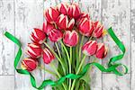 Red and yellow tulip flower decorative display with green ribbon twist over mottled distressed white wooden  background.