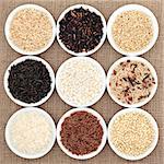 Rice grain varieties in white round porcelain bowls over hessian background.