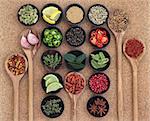 Large spice, herb and food ingredient selection in wooden bowls and spoons over cork background.