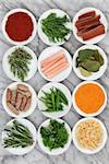 Herb and spice selection in porcelain bowls over marble background.