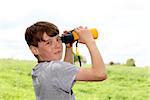 Young boy in a meadow looking through binoculars