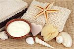 Natural skincare products of moisturising cream, exfoliating scrub, soap, sponge, towels and sea shells.