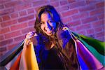 Excited Pretty Mixed Race Young Adult Woman Holding Shopping Bags with Brick Wall Background.