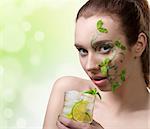 close-up portrait of pretty girl with green creative make-up and some mint leaves on the face, drinking mojito