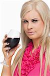 Serious blonde drinking a glass of red wine against white background