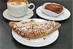 Almond Croissant French Pastry on White Plate with Cup of Latte