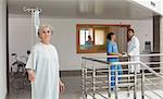 Old woman standing in the hallway in a hospital holding a drip