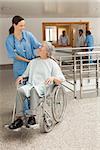 Nurse smiling at old women sitting in wheelchair in hospital corridor