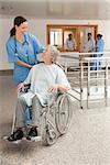 Nurse laughing with old women sitting in wheelchair in hospital corridor