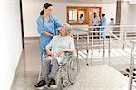 Nurse watching over old women sitting in wheelchair in hallway